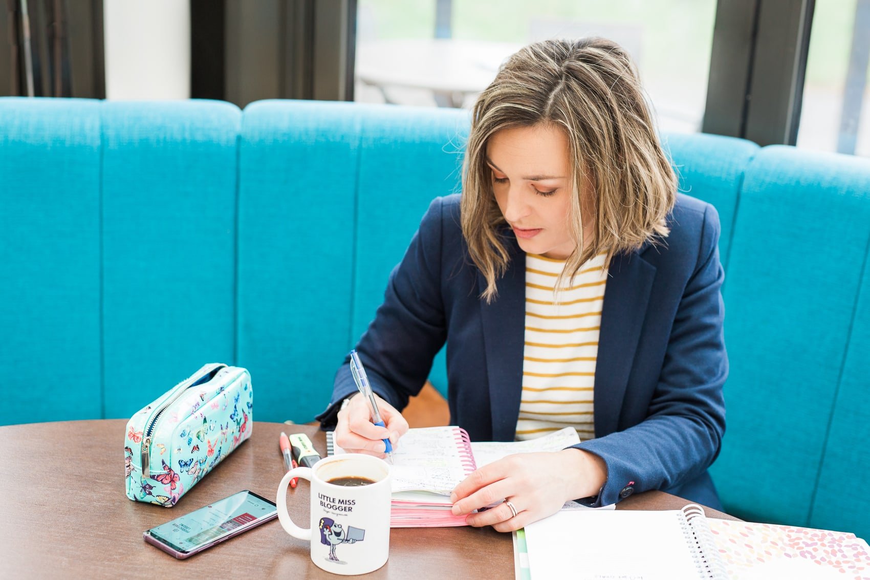 Me (Eb Gargano) writing in a notebook. In front of me is a mug which says 'Little Miss Blogger'