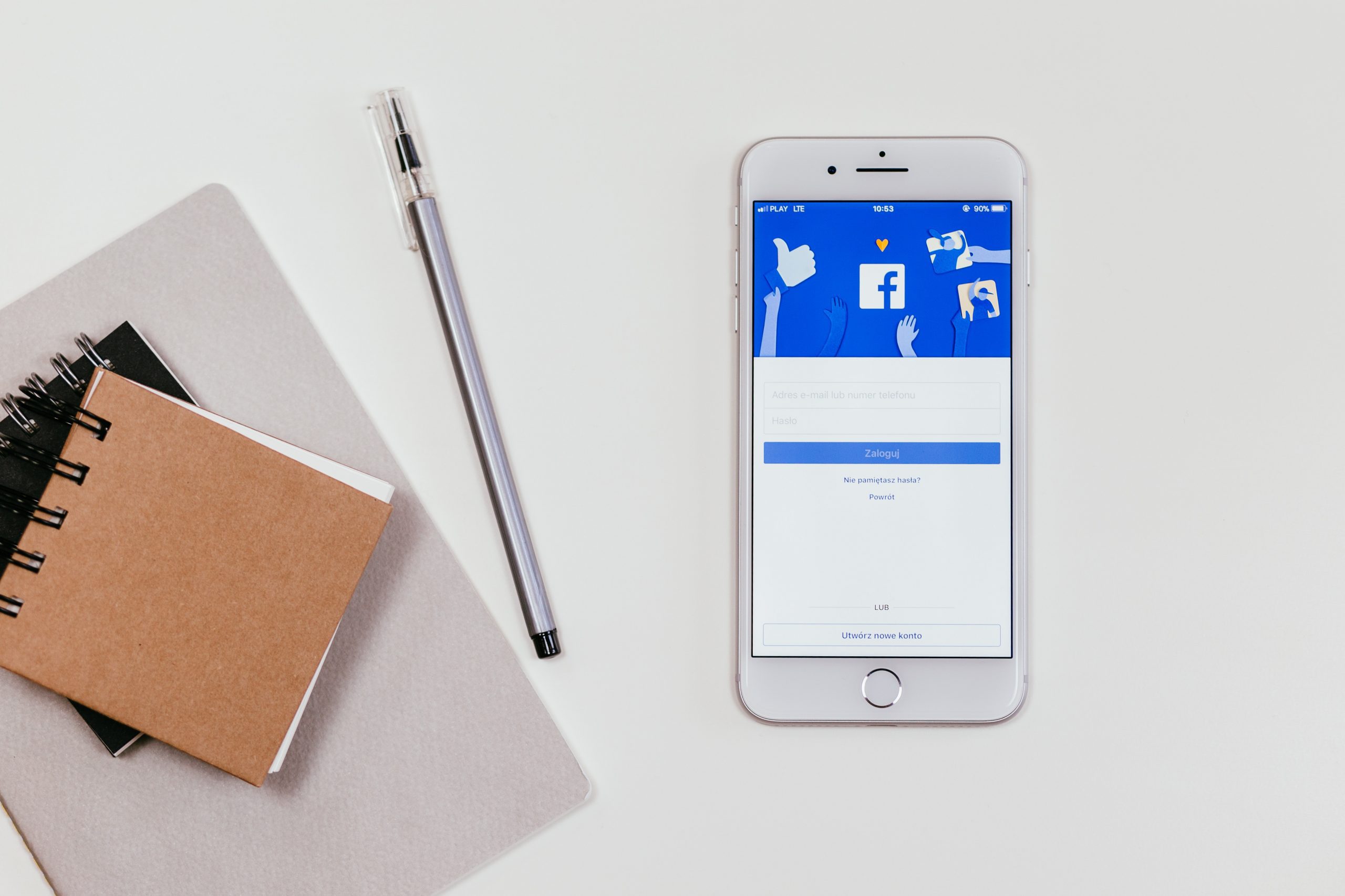 Facebook on the screen of a mobile phone next to a pen and some notebooks