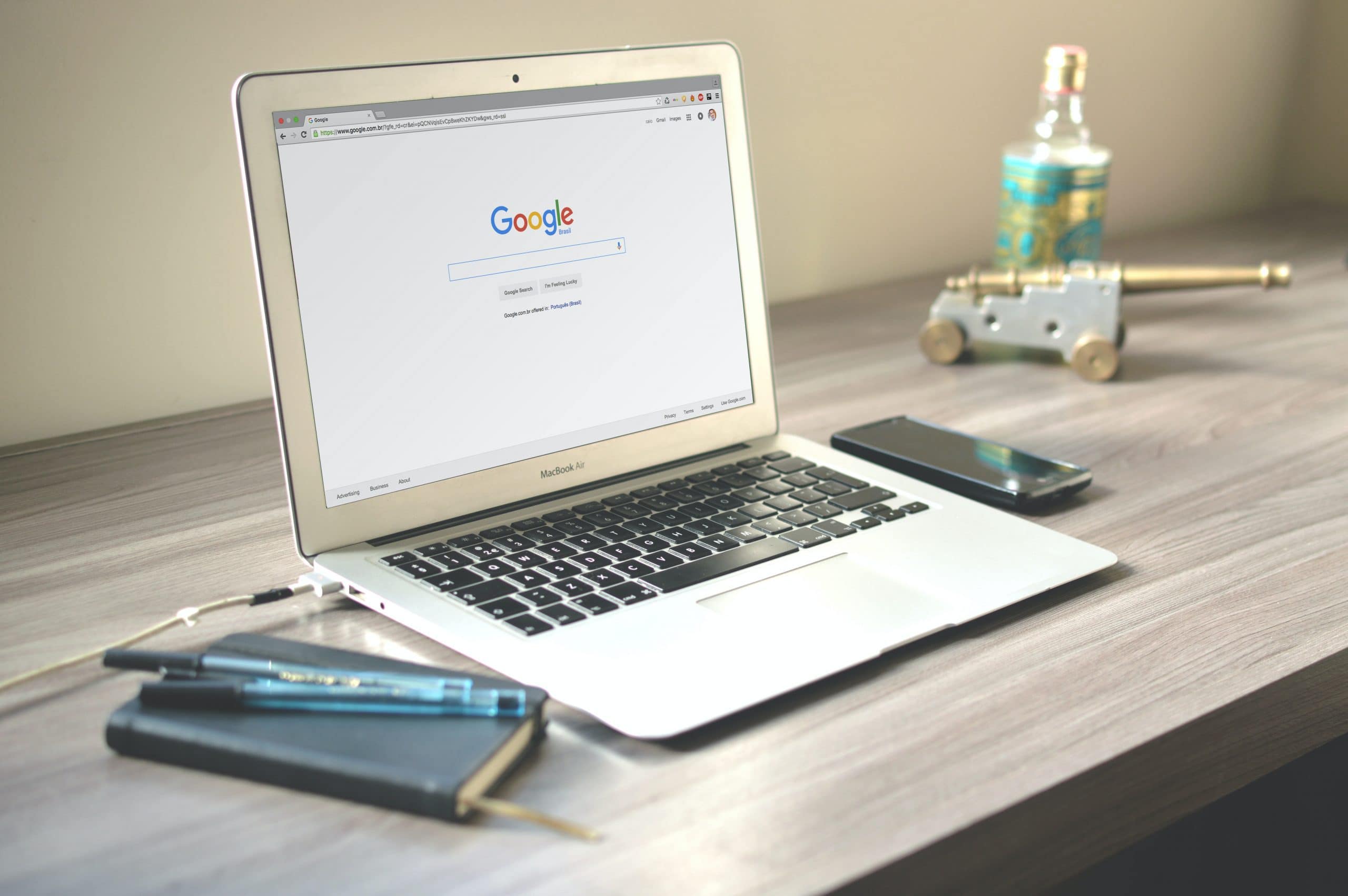 Google search open on a laptop on a desk, next to a notebook and a phone.