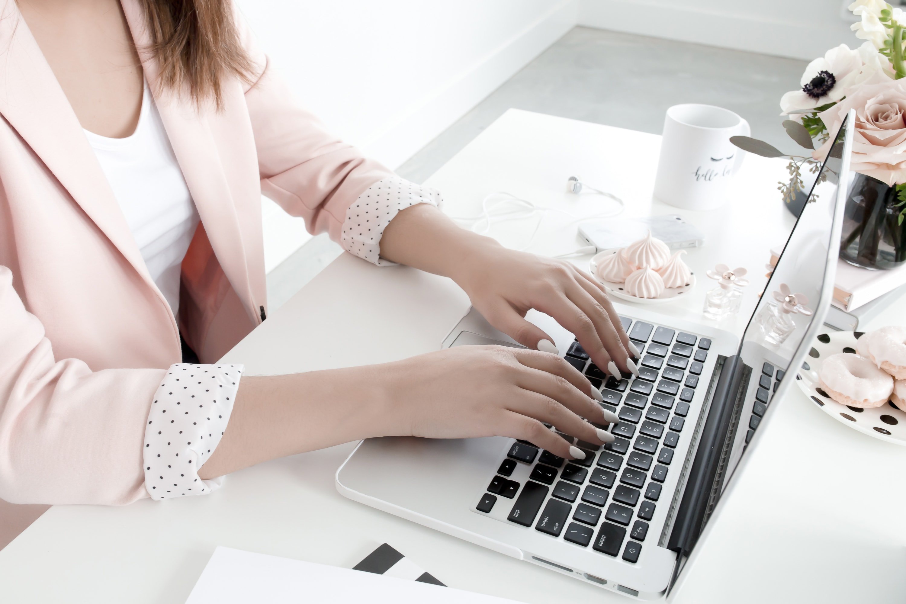 Woman in a pink jacket typing on a silver laptop