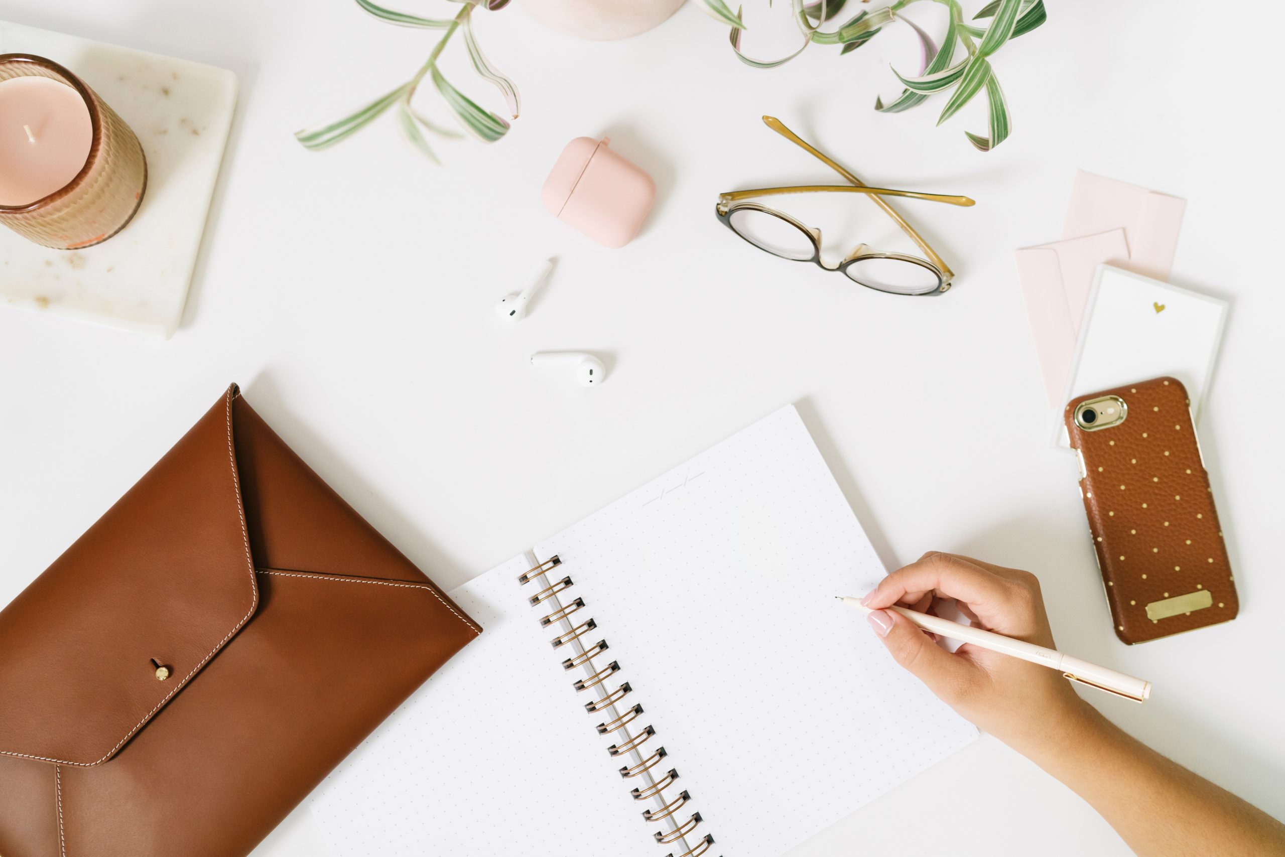 Pen poised over a blank notebook on a desk stewn with various desk items