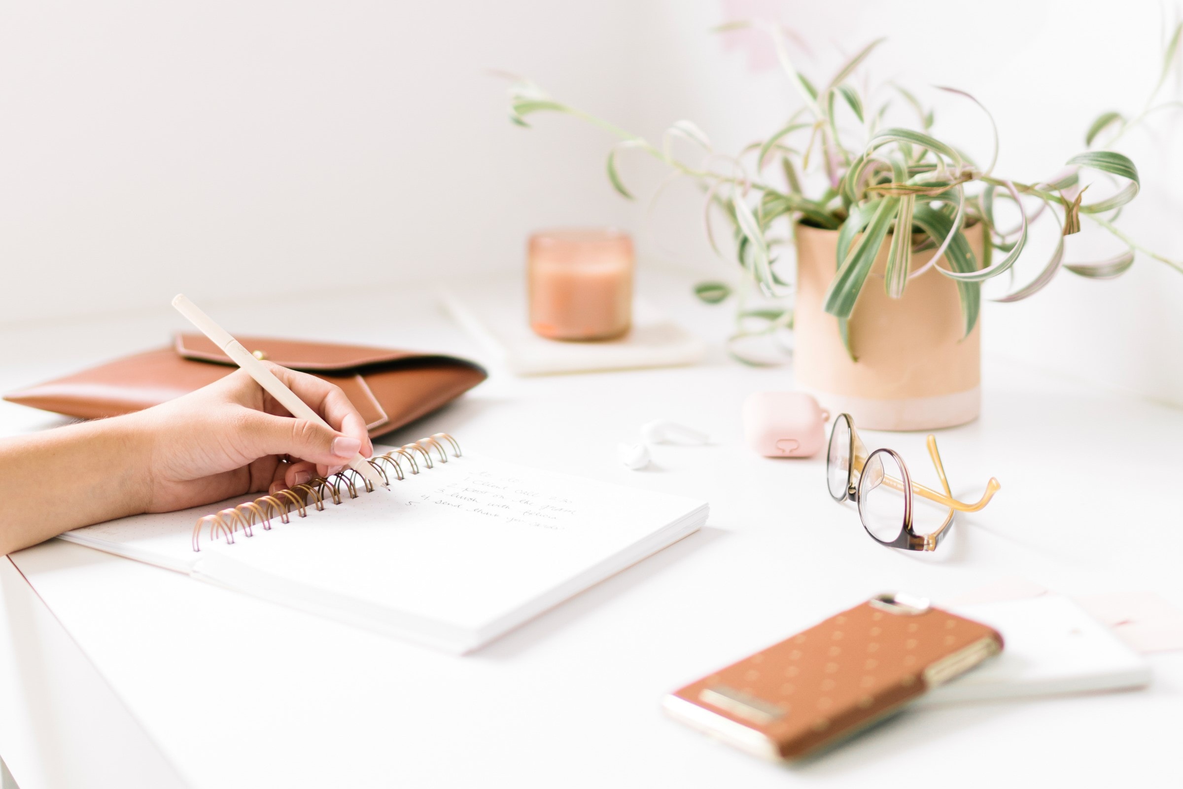 Pen poised over a blank notebook on a desk stewn with various desk items