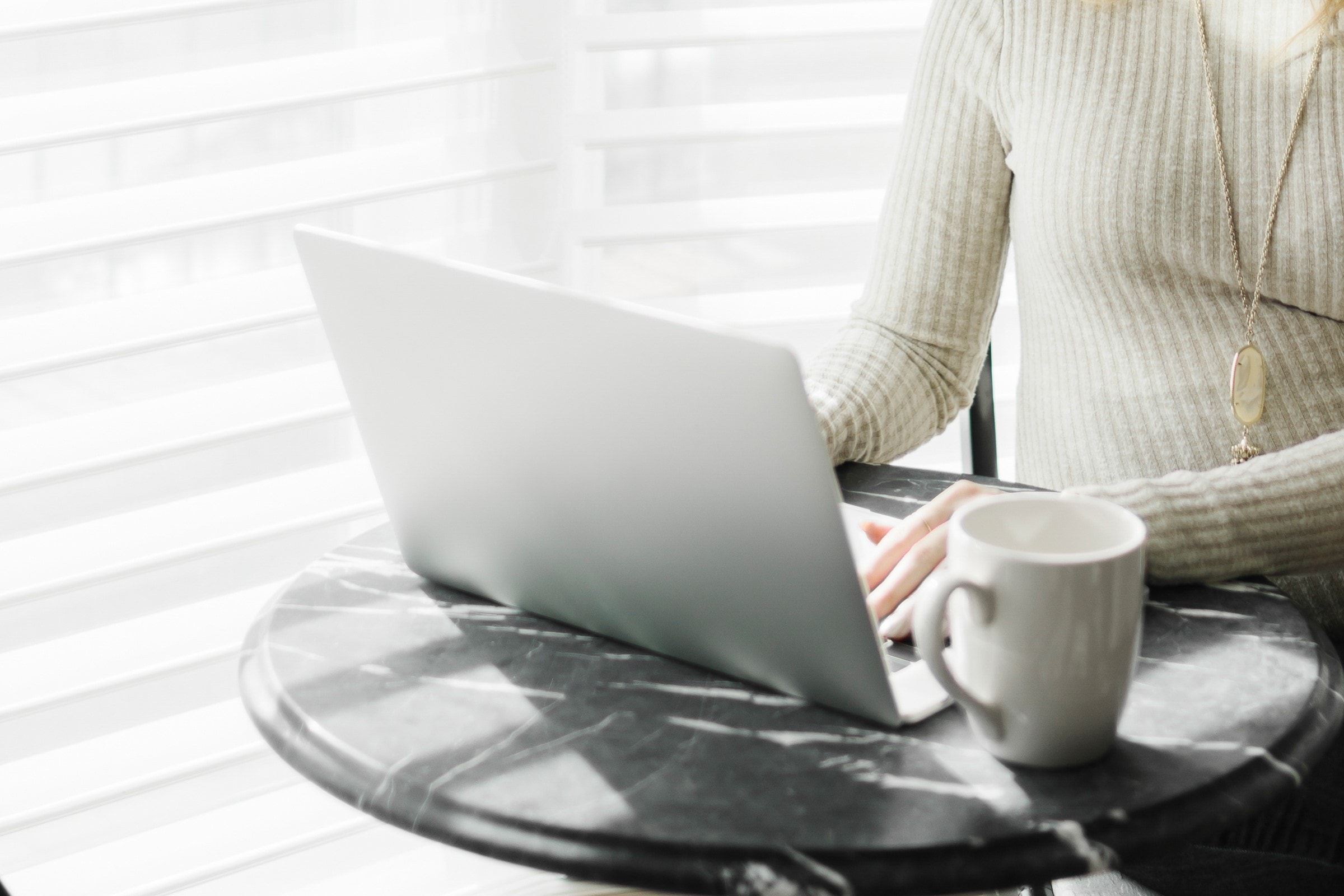 Woman sat at a coffee table typing on a silver laptop