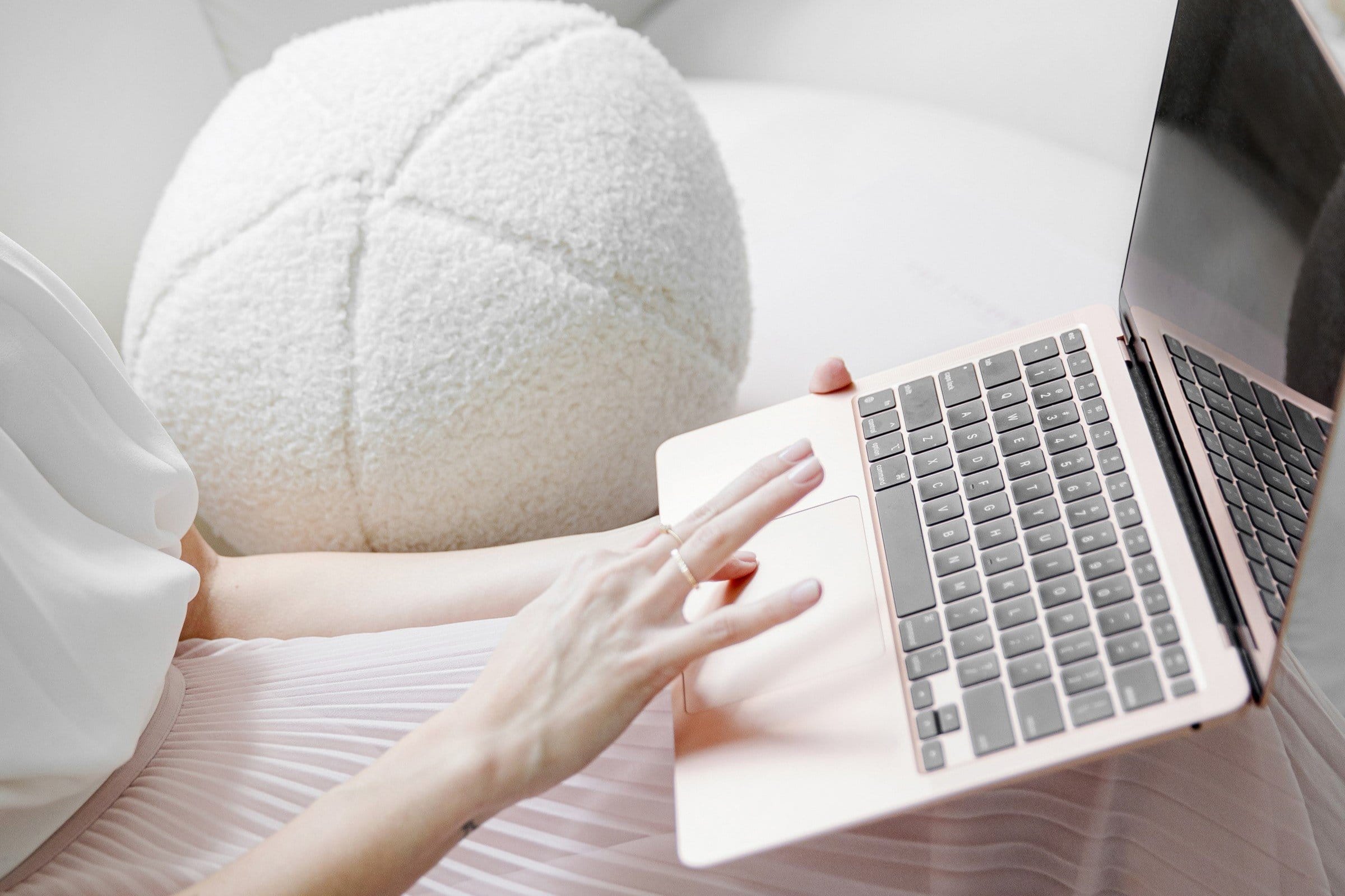 Woman sitting on a white sofa holding a rose gold computer