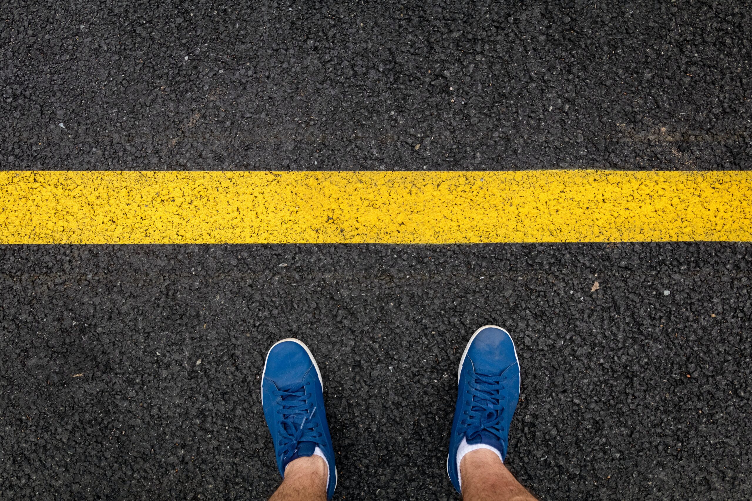 Overhead of someone's feet standing in front of a big yellow line painted onto the road